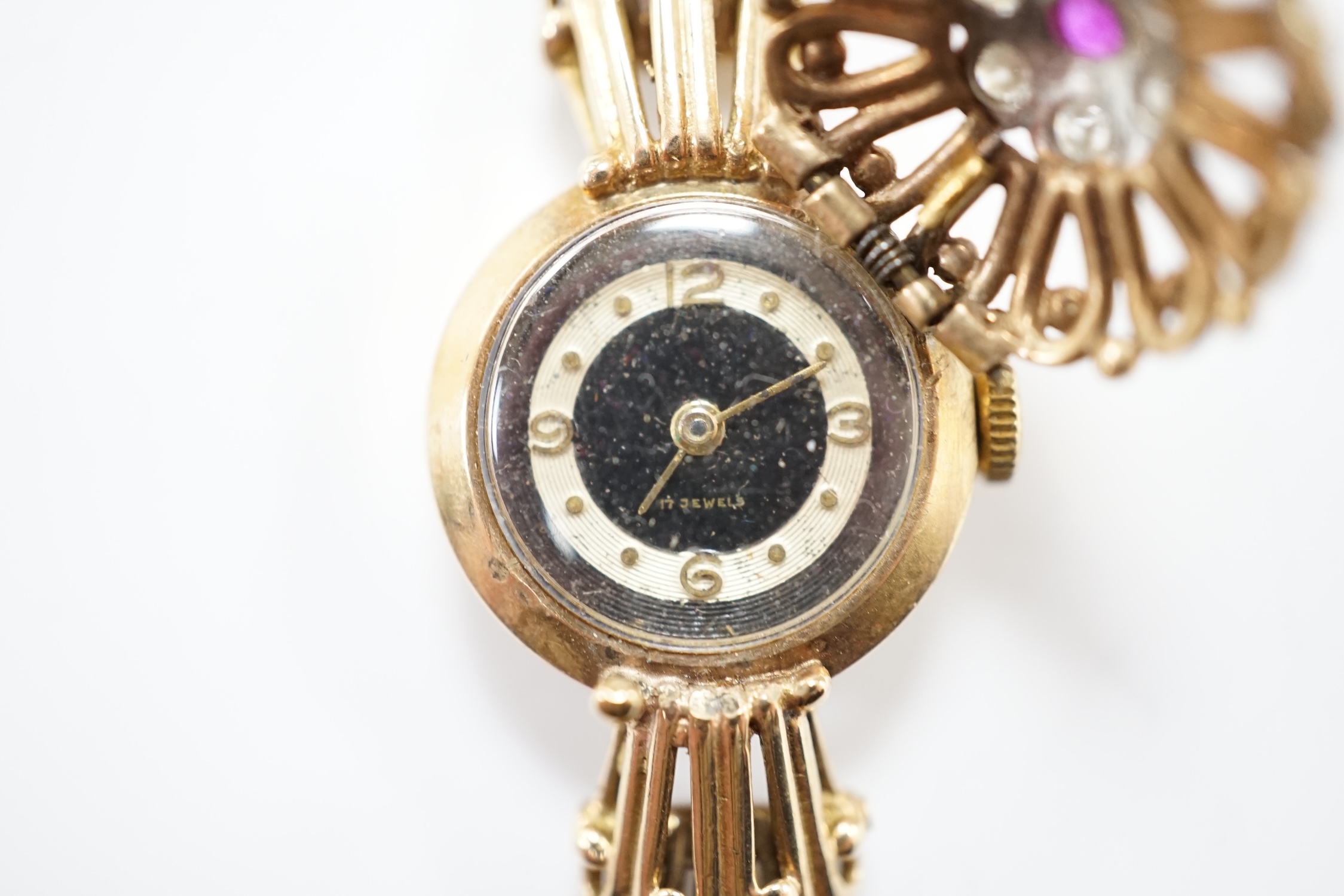 A lady's yellow metal manual wind bracelet watch, the dial with ruby and diamond cluster set hinged cover, overall length 16.3cm